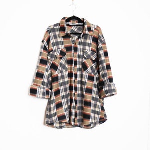 Peut inclure: Une chemise en flanelle à carreaux bruns, noirs et blancs à manches longues et fermeture boutonnée.