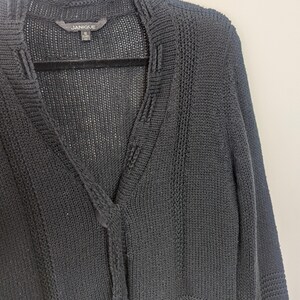 May include: Black knitted cardigan with a v-neck and button closure. The cardigan has a ribbed texture and is made of a lightweight material.