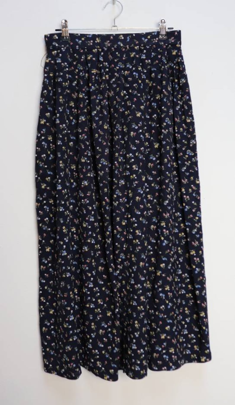 K&ouml;nnte beinhalten: Ein marineblauer Rock mit kleinem Blumenmuster. Der Rock ist plissiert und hat eine hohe Taille.