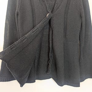 May include: Black knitted cardigan with a button fastening and long sleeves. The cardigan is made from a soft, lightweight fabric and has a relaxed fit.