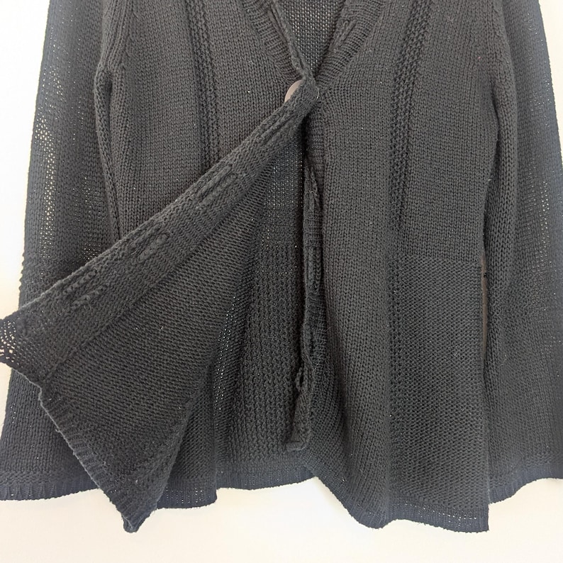 May include: Black knitted cardigan with a button fastening and long sleeves. The cardigan is made from a soft, lightweight fabric and has a relaxed fit.