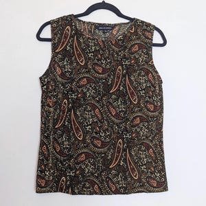 May include: Sleeveless top with a paisley pattern in shades of brown, tan, and black. The top is hanging on a black hanger. The label reads "BELLA MODA".