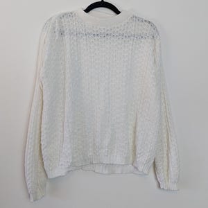 Könnte beinhalten: Weißer Strickpullover mit lockerer Passform und langen Ärmeln. Der Pullover hat ein strukturiertes, offenes Webmuster.