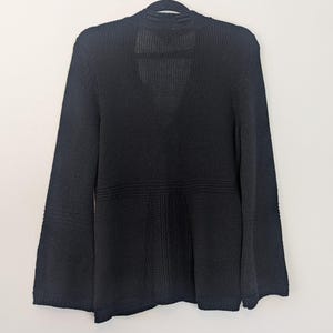 May include: A black knitted cardigan with a V-neck and long sleeves. The cardigan has a relaxed fit and a slightly flared hem.