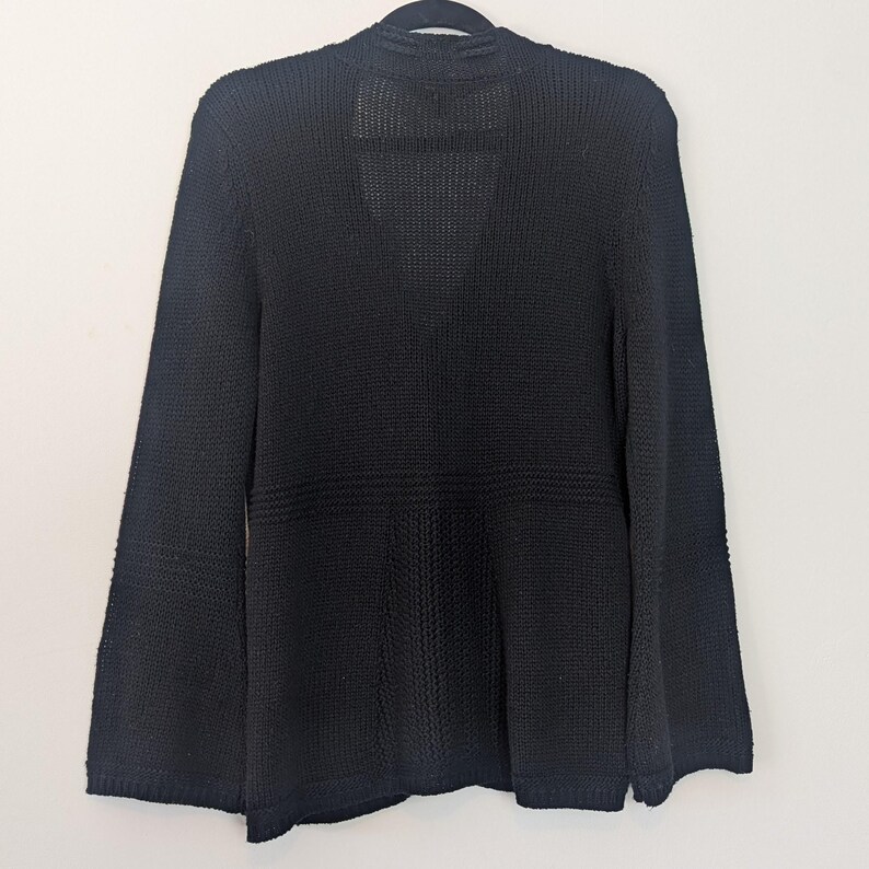 May include: A black knitted cardigan with a V-neck and long sleeves. The cardigan has a relaxed fit and a slightly flared hem.