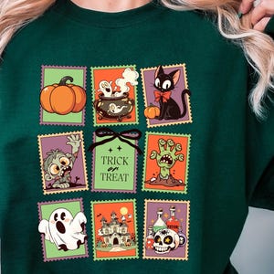 May include: Dark green sweatshirt featuring Halloween-themed postage stamp designs. The stamps depict a pumpkin, cauldron, black cat, zombie, ghost, haunted house, and skull with potion bottles. The text "Trick or Treat" is also featured.