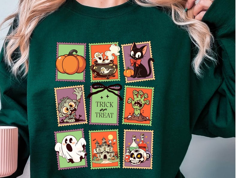 May include: Dark green sweatshirt featuring Halloween-themed postage stamp designs. The stamps depict a pumpkin, cauldron, black cat, zombie, ghost, haunted house, and skull with potion bottles. The text "Trick or Treat" is also featured.