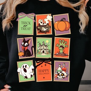 May include: Black sweatshirt featuring a colorful Halloween-themed design. The design includes various illustrations within postage stamp-like frames, such as a black cat, pumpkin, haunted house, zombie hand, ghost, cauldron, and skull with potion bottles. Text includes "Trick or Treat" and "Happy Halloween."