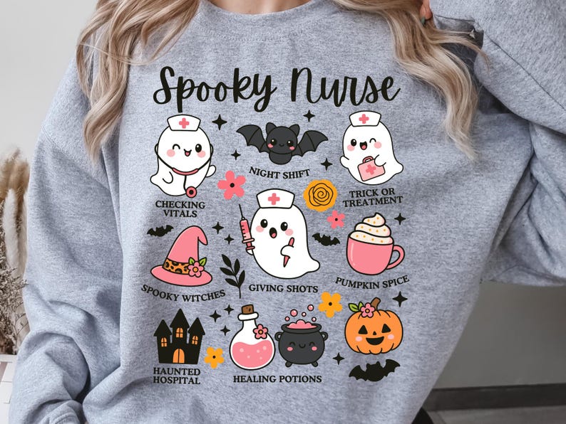 May include: A light gray sweatshirt with the words "Spooky Nurse" in a script font. The design features cartoon ghosts, bats, and Halloween-themed icons like a witch's hat and pumpkin. The phrases "Checking Vitals" and "Pumpkin Spice" are included.