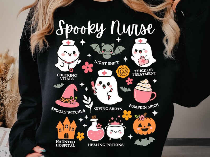 May include: Black sweatshirt with a "Spooky Nurse" graphic. The design features cartoon ghosts, bats, and Halloween-themed icons like a witch's hat, pumpkin, and potion bottles. Text includes "Checking Vitals" and "Giving Shots."