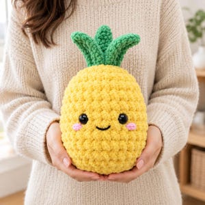 Può includere: Un peluche a forma di ananas realizzato all'uncinetto di colore giallo con foglie verdi sulla parte superiore, dotato di due occhi di sicurezza in plastica nera, una piccola bocca nera ricamata e due cerchietti rosa ricamati sulle guance.