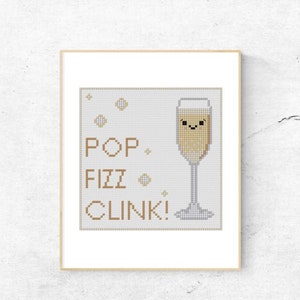 Könnte beinhalten: Kreuzstichmuster mit einer Champagnerflöte mit einem lächelnden Gesicht und dem Text "POP FIZZ CLINK!" in brauner Schrift.