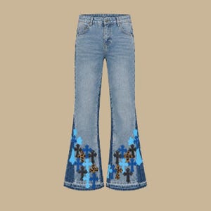 May include: Light blue denim flare jeans featuring a high-waisted design with a classic five-pocket construction. The lower legs are decorated with a repeating pattern of embroidered cross patches in shades of light blue, dark blue, and leopard print.