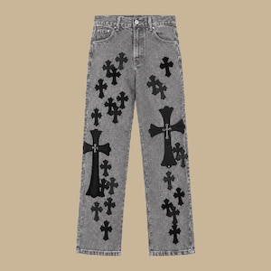 Könnte beinhalten: Graue Jeans aus Denim mit hoher Taille und Knopfverschluss. Der Stoff hat eine verwaschene, melierte graue Optik und ist mit zahlreichen schwarzen, kreuzförmigen Aufnähern in verschiedenen Größen auf den Vorderbeinen versehen.