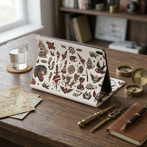May include: A white tablet case featuring a repeating pattern of traditional tattoo-style illustrations, including a black panther, a sailing ship, a dagger through a heart, a compass, swallows, a skull, and various nautical symbols.
