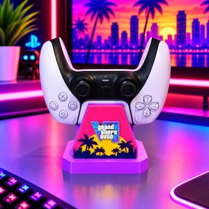 Pode incluir: Um comando de videojogos branco e preto sobre um suporte de exposição cor-de-rosa e roxo. O suporte apresenta um gráfico de palmeiras e o texto Grand Theft Auto VI numa fonte estilizada, contra um fundo de pôr do sol amarelo e laranja.