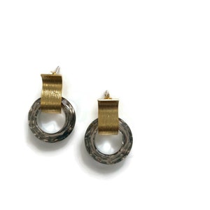 May include: A pair of gold and silver earrings with a textured, circular design. The earrings have a gold band that wraps around the circle.