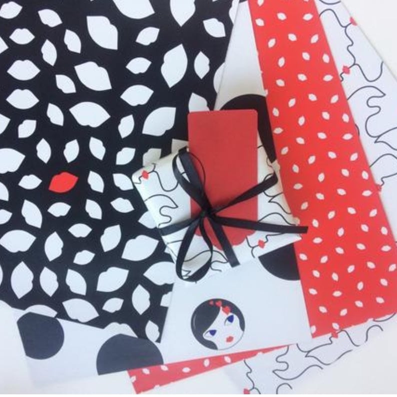 May include: Four different wrapping paper designs. One design features white lips on a black background. Another design features red dots on a white background. A third design features white dots on a red background. The fourth design features a black and white illustration of a woman's face.