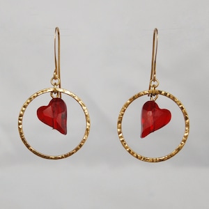 May include: A pair of gold hoop earrings with a red heart charm dangling from each hoop.