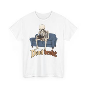 Może przedstawiać: Biały t-shirt z grafiką przedstawiającą szkielet siedzący na niebieskiej kanapie i zaglądający do pustego brązowego portfela. Pod ilustracją znajduje się napis "Dead broke" wykonany stylizowaną, postarzaną czcionką w kolorze brązowo-beżowym.
