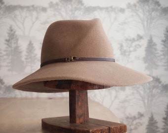 Elle: Cross front tribly crown with floppy soft brim of camel velour felt with walnut leather trim and antique brass finding