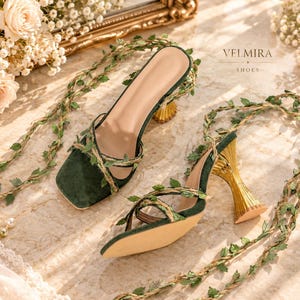 May include: A pair of dark green square-toe sandals featuring gold flared heels and thin straps wrapped in artificial green ivy vines. The brand name VELMIRA SHOES is printed in black text on the upper right side of the image.