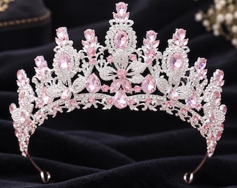 May include: A silver-toned metal tiara featuring a symmetrical arrangement of light pink teardrop and oval-shaped crystals. The piece is intricately detailed with small clear rhinestones set along the ornate, curved metal framework.