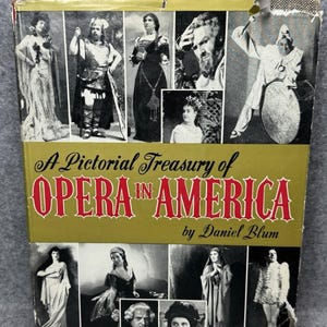 May include: A hardcover book titled A Pictorial Treasury of OPERA IN AMERICA by Daniel Blum. The gold-toned cover features a collage of black and white photographs depicting various opera performers in costumes and stage makeup.