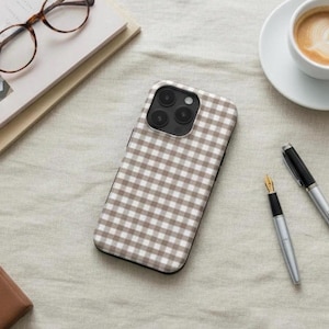 Puede incluir: Una funda para smartphone con un patrón de cuadros vichy en marrón y blanco. La funda tiene una forma rectangular con esquinas redondeadas y un recorte para un sistema de triple cámara en la parte superior izquierda del panel trasero.