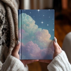 May include: A hardback journal featuring a printed design of a night sky filled with fluffy, pastel-coloured clouds in shades of pink, blue, and purple, accented by numerous bright, white, four-pointed stars scattered across the dark blue background.