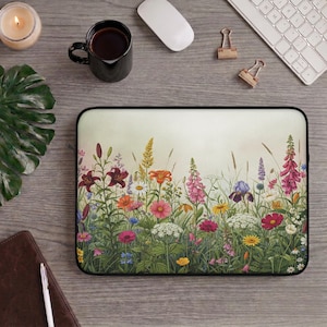 May include: A rectangular laptop sleeve featuring a vibrant, detailed botanical illustration of a wildflower meadow. The design showcases a variety of colorful blooms, including pink foxgloves, orange lilies, and white daisies, set against a soft, light-colored background.