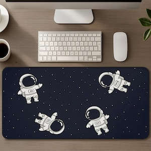 May include: A rectangular desk mat with a dark navy blue background featuring a white starfield pattern and four white astronaut illustrations. Each astronaut suit displays a keyboard key label: Alt, Space, Esc, and Ctrl on the chest area.