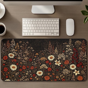 May include: A rectangular desk mat featuring a dark, moody background densely patterned with a variety of wildflowers in shades of deep red, burnt orange, cream, and muted gold. The botanical illustration covers the entire surface of the mat.