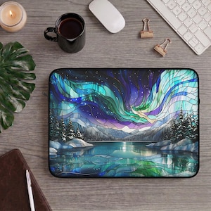 May include: A rectangular laptop sleeve featuring a stained glass style illustration of a winter landscape at night. The design displays a vibrant aurora borealis in shades of blue, purple, and teal above a frozen lake, snow-covered trees, and mountains.