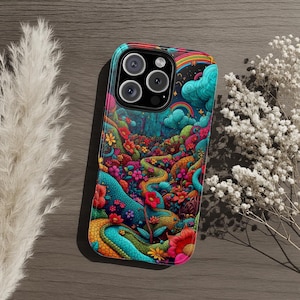 Pode incluir: Uma capa de telefone colorida com uma paisagem psicodélica vibrante com um caminho sinuoso, flores e um arco-íris. A capa tem um módulo de câmera preto e um acabamento brilhante, sobre uma superfície de madeira.