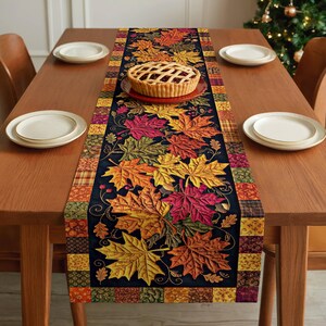 May include: A rectangular table runner featuring a central black panel decorated with vibrant, multi-colored maple leaves in shades of red, orange, yellow, and green, bordered by a patchwork pattern of various autumn-themed fabric squares.