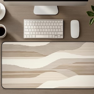 Könnte beinhalten: Rechteckiges Mauspad mit schwarzem Rand und abstraktem Design in Beige und Weiß. Das Muster ähnelt geschichteten Wellen oder Hügeln. Das Pad liegt auf einem Holzschreibtisch mit Tastatur, Maus und Monitor.