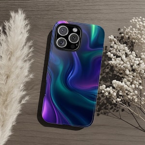 May include: A smartphone case with a vibrant, abstract design in shades of purple, teal, and blue. The case has a glossy finish and features a camera cutout. The case is lying on a wooden surface next to dried flowers.