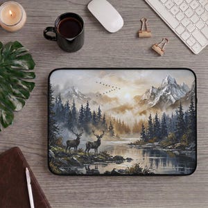 Pode incluir: Capa para laptop com uma paisagem de montanha e floresta, com dois veados perto de um lago. A ilustração é em tons de castanho, cinza e branco, com fecho de correr. A capa é retangular e protege um computador portátil.