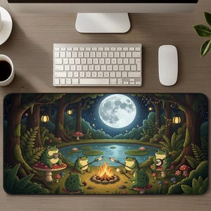 Puede incluir: Una alfombrilla de ratón caprichosa con una escena nocturna de bosque con luna llena. Varias ranas verdes se reúnen alrededor de una fogata asando malvaviscos. La alfombrilla tiene un borde negro.