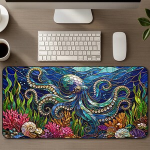 Op de afbeelding: Een rechthoekige bureaumat met een kleurrijke illustratie in glas-in-loodstijl van een octopus die onder water zwemt. Het ontwerp bevat diepblauw water, groen zeewier, felroze koraal en diverse schelpen, allemaal omlijnd met donkere lijnen.
