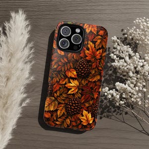 May include: A smartphone case featuring a detailed autumn-themed pattern of vibrant orange, red, and brown fallen leaves interspersed with dark brown pinecones. The design covers the entire back of the case, including the camera lens cutout area.