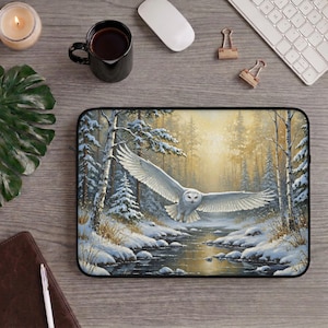 May include: A rectangular laptop sleeve featuring a printed illustration of a snowy owl in flight over a snow-covered forest stream. The scene depicts white trees, a flowing dark river, and a soft golden light filtering through the winter woods.