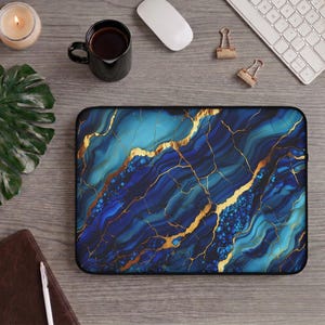 Op de afbeelding: Een rechthoekige laptophoes met een levendig blauw en groenblauw marmerpatroon met ingewikkelde gouden aders. Het ontwerp bootst het uiterlijk van gepolijste steen na met diep marineblauwe, azuurblauwe en cyaankleurige wervelingen geaccentueerd door gouden lijnen.