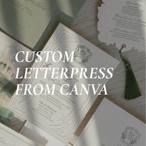 May include: A collection of cream-coloured wedding stationery featuring intricate embossed borders, elegant typography, and a decorative crest. A dark green tassel is attached to one card, and a sage green envelope is visible in the background.