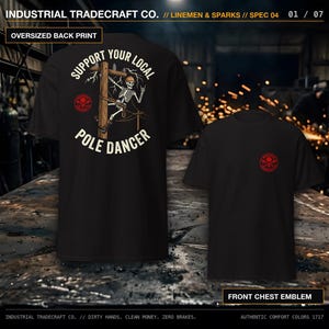 May include: A black t-shirt featuring a graphic on the back of a skeleton wearing a hard hat climbing a utility pole with the text "SUPPORT YOUR LOCAL POLE DANCER" and a small red circular emblem on the front left chest area.