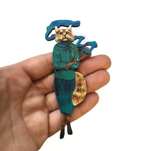 May include: A wooden cutout of a cat wearing a blue shirt and smoking a cigarette. The cat has orange and white fur and is standing on a wooden base. The cutout is made by "Pergamom Paper Goods".