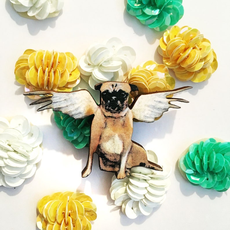 May include: A wooden pug dog with wings, painted brown and white, is surrounded by yellow, white, and green sequins.