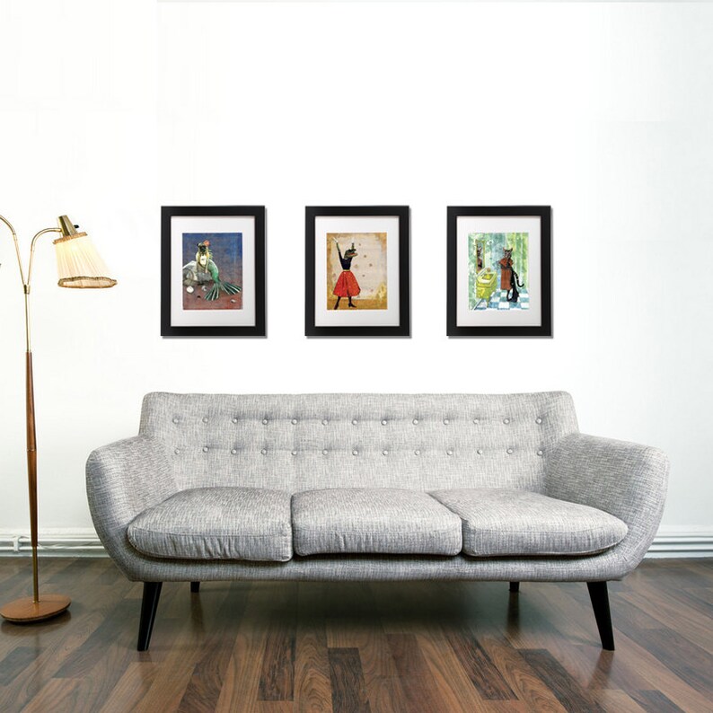 May include: Three framed illustrations of whimsical characters. The first illustration features a mermaid with green hair and a crown, sitting on a rock. The second illustration features a woman in a red dress and a black hat, dancing. The third illustration features a woman in a green dress and a black hat, holding a yellow cat.