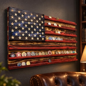 May include: A wooden wall-mounted display rack shaped like the American flag, featuring a blue canton with carved stars and horizontal red and natural wood stripes. The rack includes multiple narrow shelves designed to hold circular challenge coins.